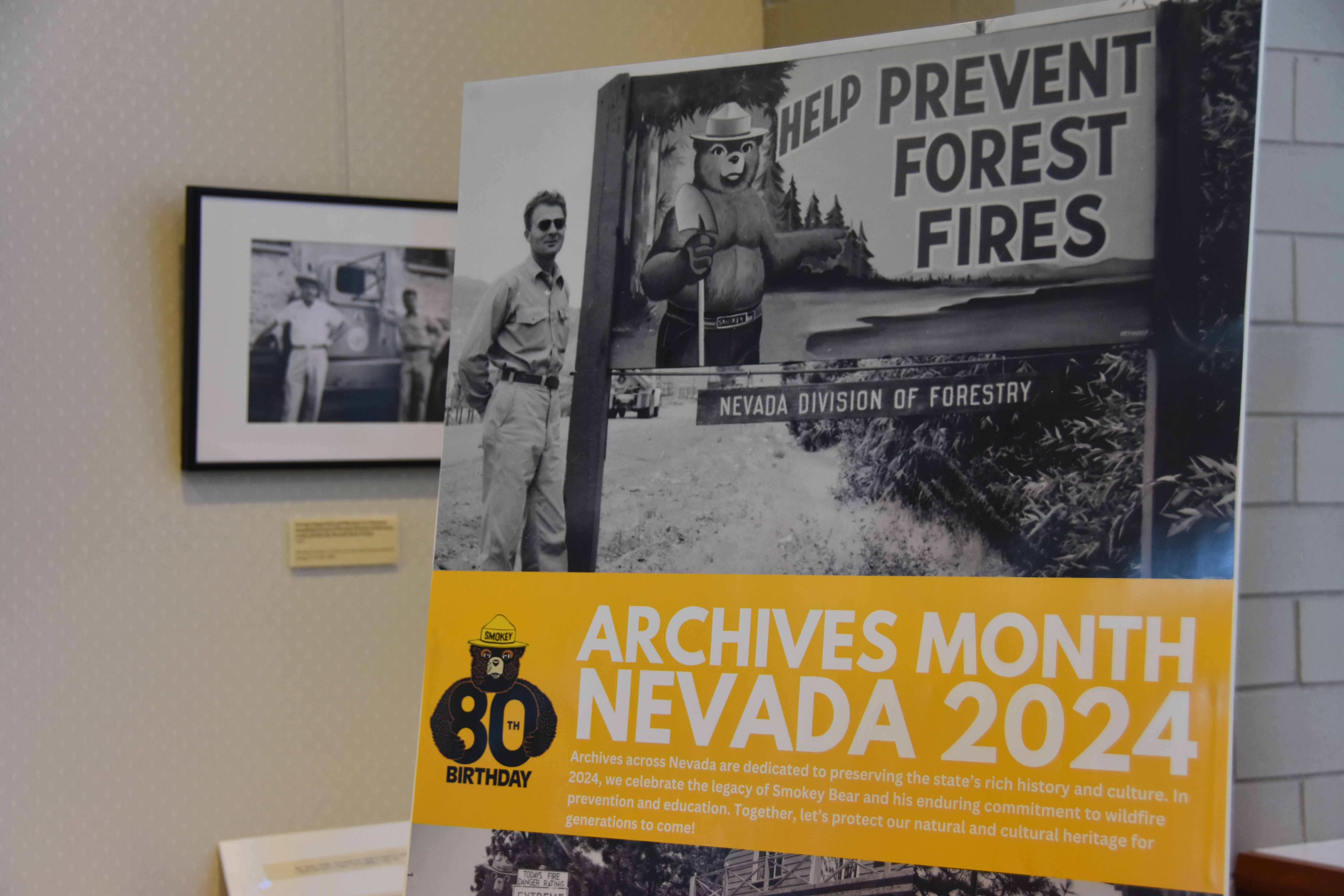 The American Archives Month Poster, showing a photograph of George Zappetini (first Nevada State Forester Firewarden) standing next to a fire prevention sign that features Smokey Bear. 